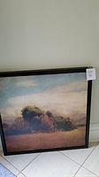 Framed landscape painting showing bushes and sky with soft pastel colors