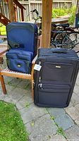 Three pieces of luggage arranged outdoors showing the front and side of two suitcases and partial view of the third.