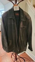 Front view of black weathered leather jacket on hanger showing collar, zipper and pockets