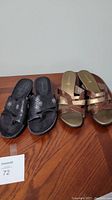 Photo shows two pairs of women's sandals side by side on a wood surface: black slip-on with toe loop and bronze crossed strap sandals.