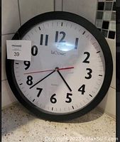 Photo of a large round La Crosse wall clock with black frame, white face, bold black numbers, and visible crazing on the face.