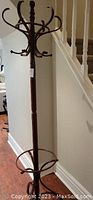 Full view of the mahogany wood stain wooden coat rack stand, showing the tall upright with multiple hooks and base ring.