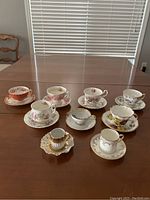 Nine assorted English china cups and saucers arranged on a wood table showing floral and gold designs.