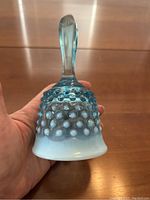 Close-up front view of the blue hobnail glass bell held in hand, showing hobnail texture and white gradient base.