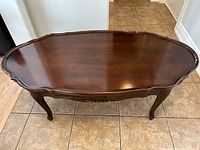 Top front view showing the oval dark wood coffee table surface with detailed carved edges and legs.