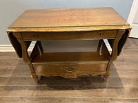 Front angle view showing top glass surface, extended drop-leaf, and lower drawers with carved details.