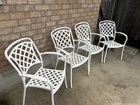 Frontal view of four white lattice-pattern iron patio chairs against brick wall