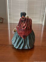 Rear view of Lady Charmian figurine showing glossy blue-green skirt and reddish cloak with bonnet