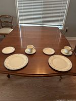 Full view of two complete 5-piece place settings including dinner plates, salad plates, bread plates, cups and saucers, arranged on a wooden table