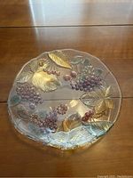 Close up of large glass fruit platter with grape and leaf embossed design with gold accent leaves.