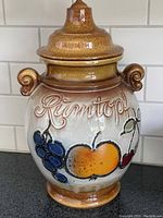 Full view of the Rumtopf jar showing shape, lid, handles, and detailed fruit decoration on the body.