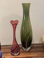 Photo showing both glass vases side by side; red and white swirled vase to the left with ruffled top, green vase to the right tall with spiral white swirls.