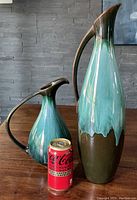 Two Blue Mountain Pottery ewers displayed beside a can of Coke to indicate size. The ewers have a retro glaze in green, blue and brown shades, with tall slender and shorter rounded shapes.