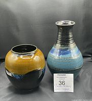 Two vintage signed studio art pottery vases, one taller with blue and black glaze and one shorter with earthy crackled mustard yellow and blue glaze.