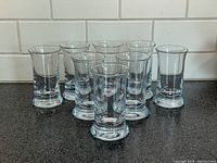 Eight clear glass tumblers arranged in two rows on black countertop, white subway tile background, showing size and shape.