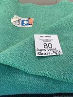 Photo showing a folded retro green wool blanket with Ayers tag and a note with size 80x80.