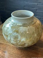 Side view of the pottery vase showing crystalline glaze and floral patterns, with a wooden table and dark background