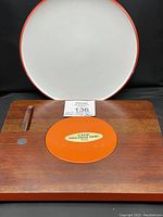 Photo showing the top view of the Dansk Købenstyle chop plate with white surface and orange trim, along with the wooden Sears Warner cheese board showing the orange enamel insert with sticker.