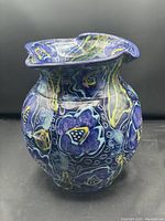 View of colorful floral-patterned pottery vase with flared rim and bulbous shape on dark background.