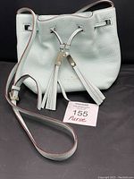 Front and full view of baby blue Kate Spade cinch top bucket purse with tassels and adjustable shoulder strap.