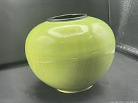 Front view of a round lime green Raku vase with smooth glossy glaze and faint horizontal lines, showing skipped glaze specks.