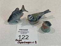 Photo showing all three Royal Copenhagen porcelain figurines: Blue Tit bird, American Perch fish, and a smaller bird figurine