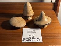 Photo of complete set of 3 hand-carved wood mushrooms on wooden surface, including auction lot card for identification
