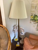 Floor lamp with lampshade standing beside two porcelain figurines on a small table.