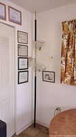Full view of the tall floor lamp positioned in a corner near certificates and a window with a floral curtain.