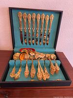 Full view of the open box containing gold plated flatware arranged upside down on upper tier with knives and the lower tier with all other utensils neatly organized