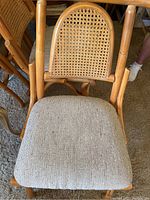Close-up of a vintage rattan chair showing woven cane back and light fabric upholstered seat with signs of wear and dirt.