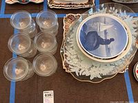 Top view presenting six frosted glass shrimp serving dishes and stack of ornate platters showing fruit and floral designs.