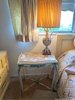 Nightstand with ornate legs and carved detailing, topped with marbled stone surface. Lamp placed on top with lampshade visible.