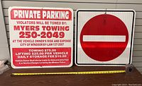 Photo of two metal signs including a Private Parking sign and a No Entry sign laid flat on a wooden table with measuring tape.