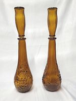 Two tall amber glass decanter vases with large stoppers, standing upright against a plain background.