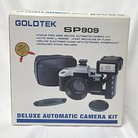 Photo of the Goldtek SP909 Deluxe Automatic Camera Kit box showing key features including focus free, auto wind and rewind, deluxe electronic flash, and shoulder strap included.