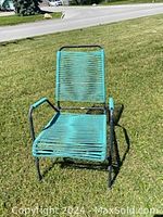 Vintage lawn patio chair with black metal frame and green plastic webbing on a grass lawn. Shows full front view of chair.