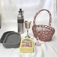 Complete lot with all six items displayed: water bottle, silver plated chalice, basket, blown glass angel, seed packet, and kitchen sink accessories.