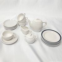 Full Ikea Duktig white porcelain children's tea set for four, including teapot, sugar bowl, creamer, four cups, saucers, and plates with navy blue rim and plain white plates.