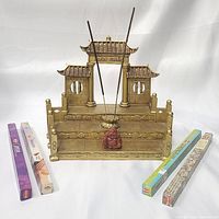 Golden resin Asian temple incense burner with two incense sticks inserted and goldstone Buddha in front, accompanied by four boxes of incense sticks.