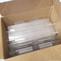 Box containing multiple clear acrylic slat wall shelves stacked, showing the built-in hangers on top for slat wall mounting.