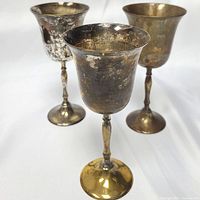 Front angled view showing all three silver-plated brass chalices with tarnish and wear visible on surfaces.