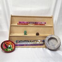 Image of wooden display shelf with five packs of stick incense, small green owl and brown turtle stone figurines, Mexican ceramic bowl, and gray stone bowl.