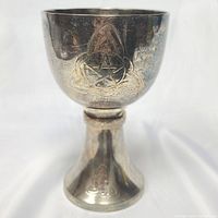 Front view of large silver chalice showing engraved Celtic triquetra and pentacle designs with visible tarnishing on the surface.