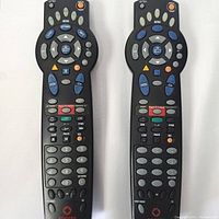 Front view of two Nextbox black TV remotes with all buttons visible
