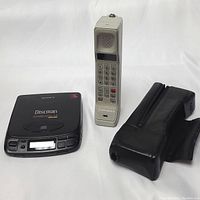 Sony Discman black portable CD player, Motorola beige brick phone, and black leather carrying case side by side on white background.
