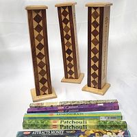 Three wooden incense tower burners with diamond inlay patterns and five packs of stick incense placed in front. One burner is slightly larger with a cone incense holder feature. Scents include jasmine, opium, lemongrass, patchouli, and attracts money.