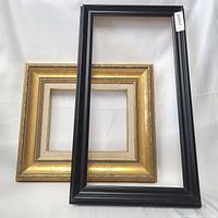 Two wooden picture frames, one gold with fabric mat and floral pattern, one brown with ribbed texture.