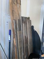 Eleven barn boards leaning against a garage wall, showing varied widths and lengths with natural and weathered wood textures.