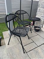 Two black metal chairs and one round bistro table on stone patio, paint chipping on chairs